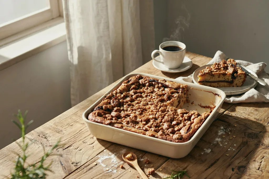 A whole grain coffee cake with a thick streusel topping, one corner slice lifted out showing a cinnamon ribbon through the crumb.